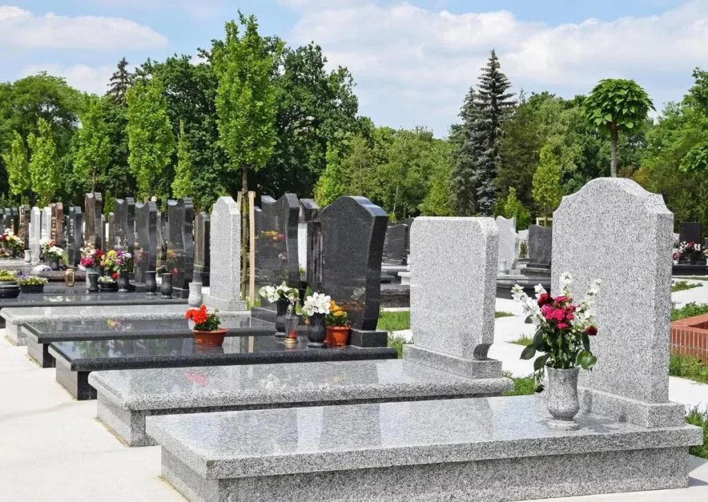 Monuments funéraires en granit alignés dans un cimetière paysagé.